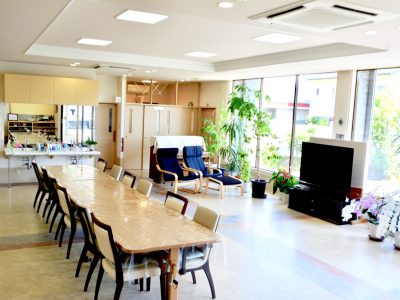 [デイルーム大きな窓から陽ざしがいっぱいに差し込んで、光あふれる、開放的なスペースです。ひとつのテーブルを囲んで、お話やお食事の時間を楽しんでいただきます。窓からの眺めを楽しむ、本を読むなど、ご自由にお過ごしください。]